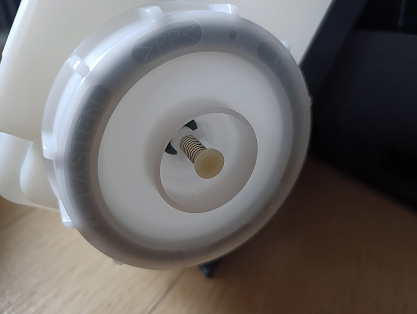 Korek zbiornika w oczyszczaczu Sharp z widocznym zaworem sprężynowym sterującym wypływem wody